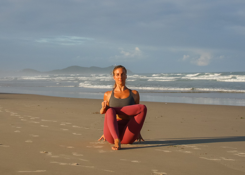 Yoga teacher in seated variation of pigeon pose (Eka pada raja kapotasana) on the beach
